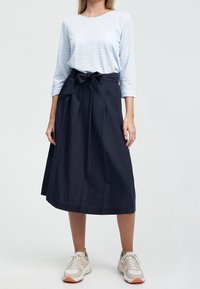 Blå och vit randig långärmad topp i kombination med en mörk marinblå högmidjad kjol med knytbälte och sidofickor. Avslutad med sneakers.