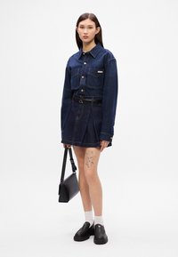 Τζιν πουκάμισο με δύο τσέπες στο στήθος, συνδυασμένο με φούστα τζιν με πτυχώσεις. Μαύρη τσάντα χειρός, λευκές κάλτσες και χοντρές μαύρες παπούτσια ολοκληρώνουν την εμφάνιση.