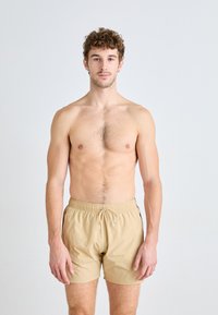 Shorts de bain beiges avec une taille élastique et un cordon de serrage. Le matériau semble léger, avec des accents latéraux en noir.