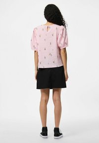 Camicia rosa con motivo floreale, maniche a palloncino e schiena con apertura a chiave, abbinata a una gonna nera e sneaker alte nere.