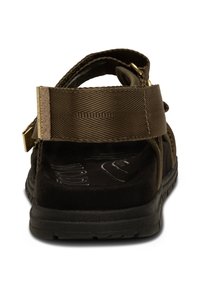 Brown sandal featuring textured fabric straps, gold hardware accents, and a cushioned black insole. Includes adjustable straps for fit.