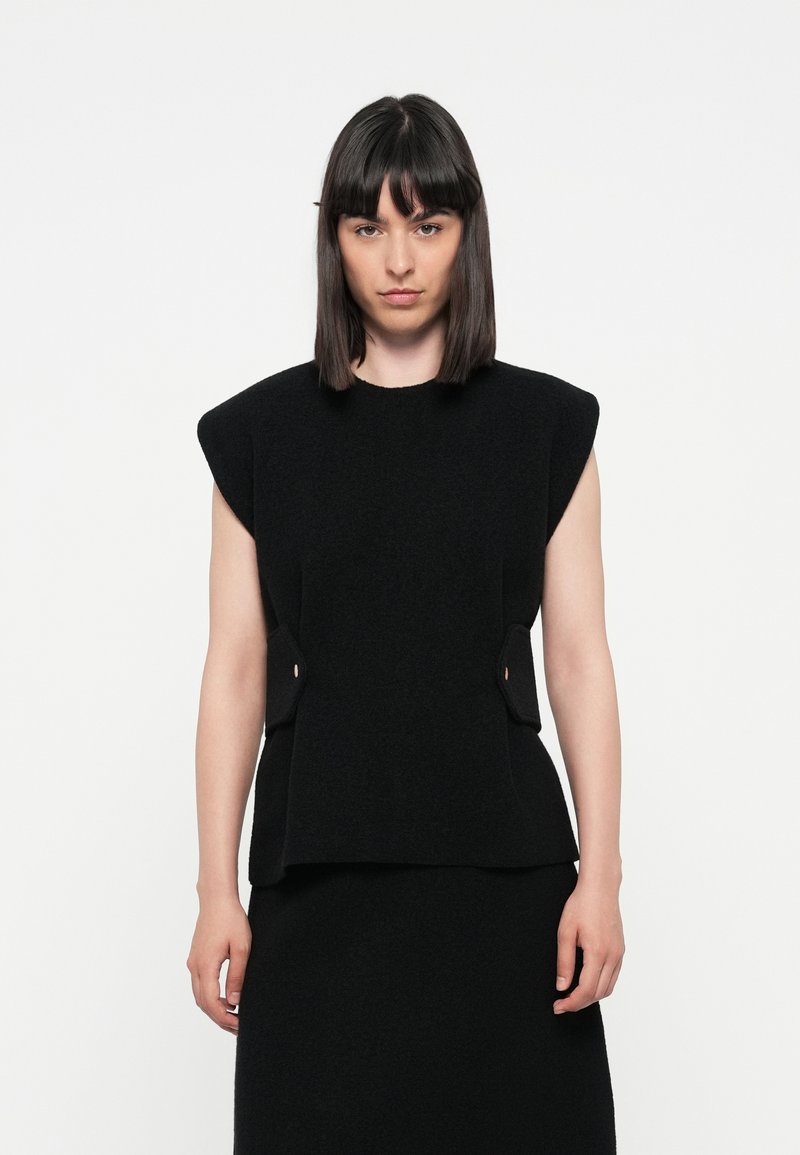 Black sleeveless top with a structured design, featuring unique side accents, made from textured fabric, pairing with a matching skirt.