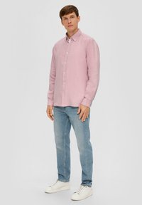 Helles rosa Langarmhemd mit Button-down-Kragen, kombiniert mit hellblauen Jeans und weißen Sneakers. Das Hemd hat eine glatte Textur.