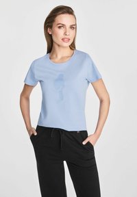 Jasnoniebieska bawełniana koszulka z okrągłym dekoltem, krótkimi rękawami i subtelnym nadrukiem logo z przodu, zestawiona z czarnymi spodniami dresowymi.