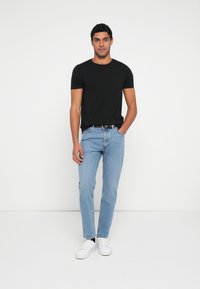 Svart t-skjorte med korte ermer, lyseblå jeans med rette ben og hvite joggesko. Enkel design, ledig passform, minimal dekorasjon.