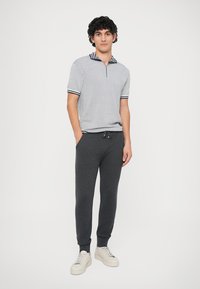 Polo riscado com meia cremalheira, combinado com calças de jogging cinza-escuras e ténis brancos. Material de algodão com punhos e colarinho canelados.