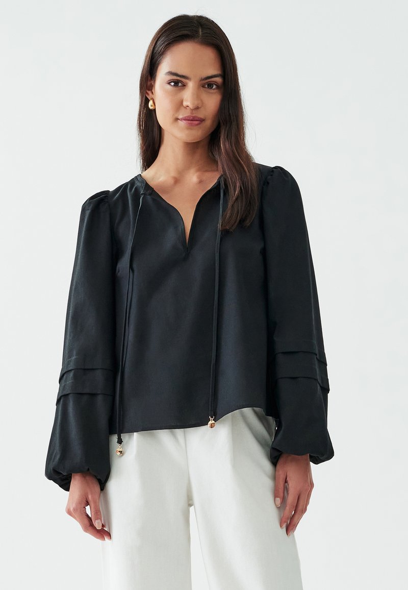 Blusa nera realizzata in tessuto morbido, con scollatura a V, maniche a sbuffo con dettagli arricciati e lacci regolabili con accenti dorati.