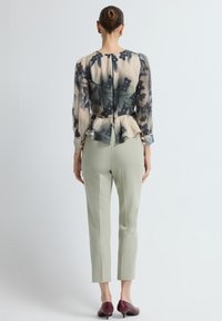 Bloemenpatroon, doorzichtige blouse met lange mouwen en een peplumzoom, gecombineerd met slanke, lichtgroene broeken en bordeauxrode hakken.