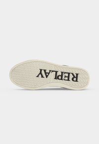 Semelle d'une sneaker blanche avec un motif de grip texturé et le mot "REPLAY" imprimé en grandes lettres noires sur le dessous.