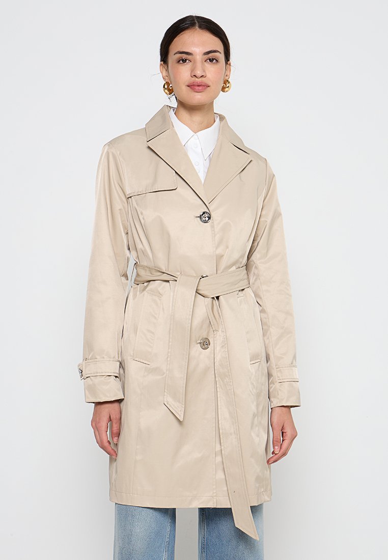 Trench-coat beige avec une taille cintrée par une ceinture, grand col et fermeture à boutons; dispose de poches latérales et de poignets à boutons. Texture lisse.