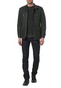Donkergroene gewaxte jacket met een bruine kraag, rits aan de voorkant, vier voorzakken en een casual pasvorm. Gecombineerd met een donkere spijkerbroek en zwarte schoenen.