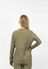 Langarmshirt van olijfgreen geribbeld materiaal met een ronde halslijn, getailleerde pasvorm en duimgaten bij de manchetten, gedragen met bijpassende onderkleding.