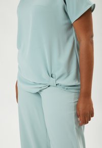 Top azzurro chiaro a maniche corte con dettaglio nodoso in vita, abbinato a pantaloni coordinati, realizzati in tessuto morbido e leggero.