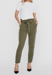 Pantalones de color verde oliva, de cintura alta con un cinturón atado, bolsillos delanteros y piernas ajustadas; textura suave y tejido de mezcla de algodón.