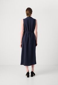 Vestido azul marino sin mangas con cintura ceñida, que presenta un corte largo y recto con sutiles rayas verticales. Zapatos de tacón alto negros completan el look.