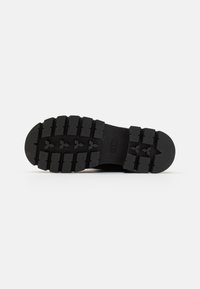 Black rubber outsole with deep treads and defined grooves for traction. Rounded toe and flat design suitable for outdoor activities.