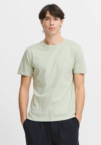 Tricou din bumbac verde deschis, cu mâneci scurte, guler rotund și o croială lejeră. Remarcabil pentru textura sa netedă și designul minimalism.