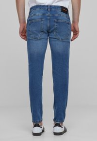 Jeans de mezclilla azul con un corte recto, cinco bolsillos y una etiqueta en la cinturilla. La tela tiene una textura suave con un lavado medio.