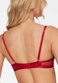 Red bra featuring a sheer back, adjustable straps with gold hardware, and a lace accent along the band for added detail.