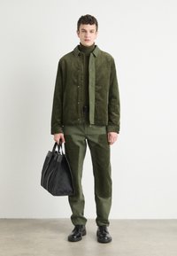 Olive green corduroy jacket over matching turtleneck and pants; black leather shoes; holding a textured black tote bag. Clean lines, minimal design.
