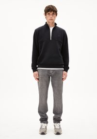 Sweatshirt en polaire marine avec col zippé, associé à un jean en denim gris clair. Le modèle porte des baskets blanches et grises. Design simple, coupe décontractée.