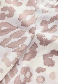 Leopardenmusterstoff in sanften Beige- und hellrosa Tönen, mit einer strukturierten Oberfläche und markanten, unregelmäßigen Mustern.