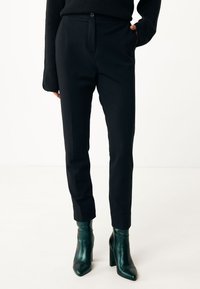 Pantalones negros ajustados de corte slim, con cierre de botón y bolsillos laterales. Combinados con botas de tobillo verde brillante.