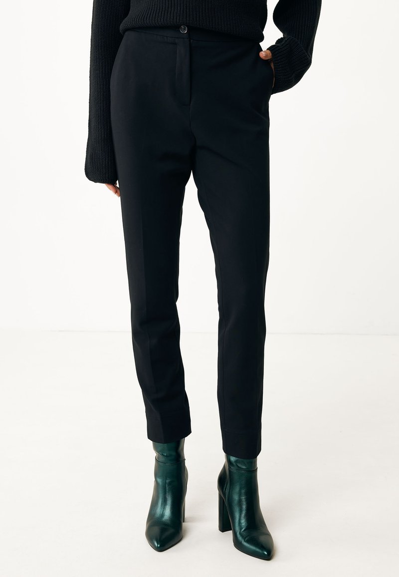 Pantalones negros ajustados de corte slim, con cierre de botón y bolsillos laterales. Combinados con botas de tobillo verde brillante.
