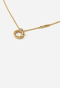 Goldkette mit einem gedrehten Schlaufenanhänger, der mit kleinen klaren Steinen und einem "GUESS"-Tag verziert ist. Elegantes Design mit glänzendem Finish.