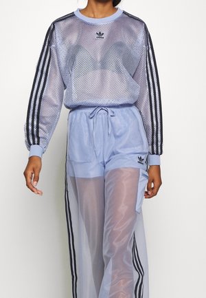 Vrouw draagt lichtpaars Adidas mesh langärmelig top en doorschijnende trainingsbroek met zwarte strepen en logo's.