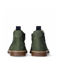 Un paio di stivaletti alla caviglia in suede verde con suole marroni, vista posteriore che mostra i dettagli cuciti e le linguette di tessuto nere.