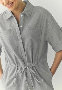 Gestreepte shirtjurk in zwart en wit, met een kraag, knoopsluiting, elastische taille en twee borstzakken. Zachte stof, ontspannen pasvorm.