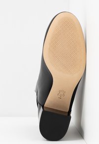 Semelle de bottine en cuir noir avec avant en cuir fauve texturé, talon noir solide et indication de taille 8M visible sur la zone lisse de l’arche.
