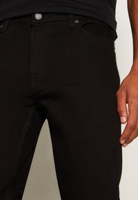 Černé džíny z denimu s úzkým střihem, standardním pětikusovým stylem, kovovým zapínáním na knoflík a decentními švy.