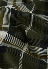 Grün-schwarz kariertes Gewebe mit weißen und gelben Akzenten. Strukturierter Webstoff mit diagonalen Linien, die Tiefe und Muster erzeugen. Weicher Fall.