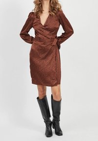 Vestido envolvente marrón con estampado de leopardo, mangas largas y detalle de cintura atada. Combinado con botas negras hasta la rodilla. Textura suave de satén.
