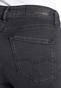 Μαύρο τζιν παντελόνι με λεία υφή, διαθέτοντας μια χαρακτηριστική σχεδίαση πίσω τσέπης και μια μαύρη δερμάτινη ετικέτα μάρκας στη μέση.