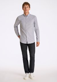 Button-up shirt with light gray and navy stripes, long sleeves, and a standard collar, paired with black pants and white sneakers.