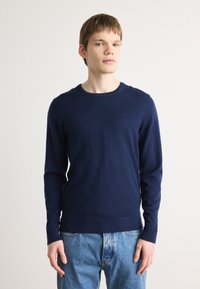 Pulover lung, cu mânecă lungă, de culoare bleumarin, cu decolteu rotund, confecționat dintr-un material moale, având un logo subtil pe piept și manșete ribbate.