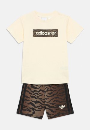 Kremowy t-shirt Adidas z krótkim rękawem i logo w kamuflażu oraz pasujące brązowo-czarne spodenki w kamuflażowy wzór z logo Adidas.