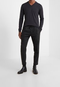 Pullover nero a maniche lunghe con scollatura a V abbinato a pantaloni a quadri neri con vita elasticizzata e taglio alla caviglia, indossato con stivali neri.
