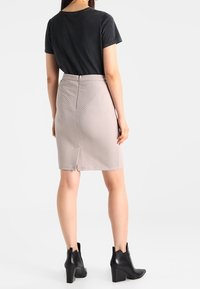 Top negro de manga corta combinado con una falda beige clara de longitud a la rodilla que presenta un patrón de espiga. Botines negros completan el atuendo.