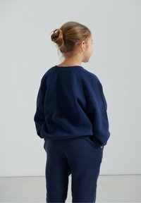 Laivastonsininen pusero pyöreällä kaula-aukkolla ja pitkillä hihoilla, yhdistettynä samanvärisiin collegehousuihin. Pehmeä, teksturoitu kangas ja rento istuvuus.