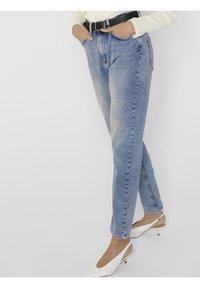 Jeans de mezclilla azul claro con un corte relajado, bolsillos delanteros y trabillas para cinturón. Combinados con tacones blancos y un suéter ajustado color crema.