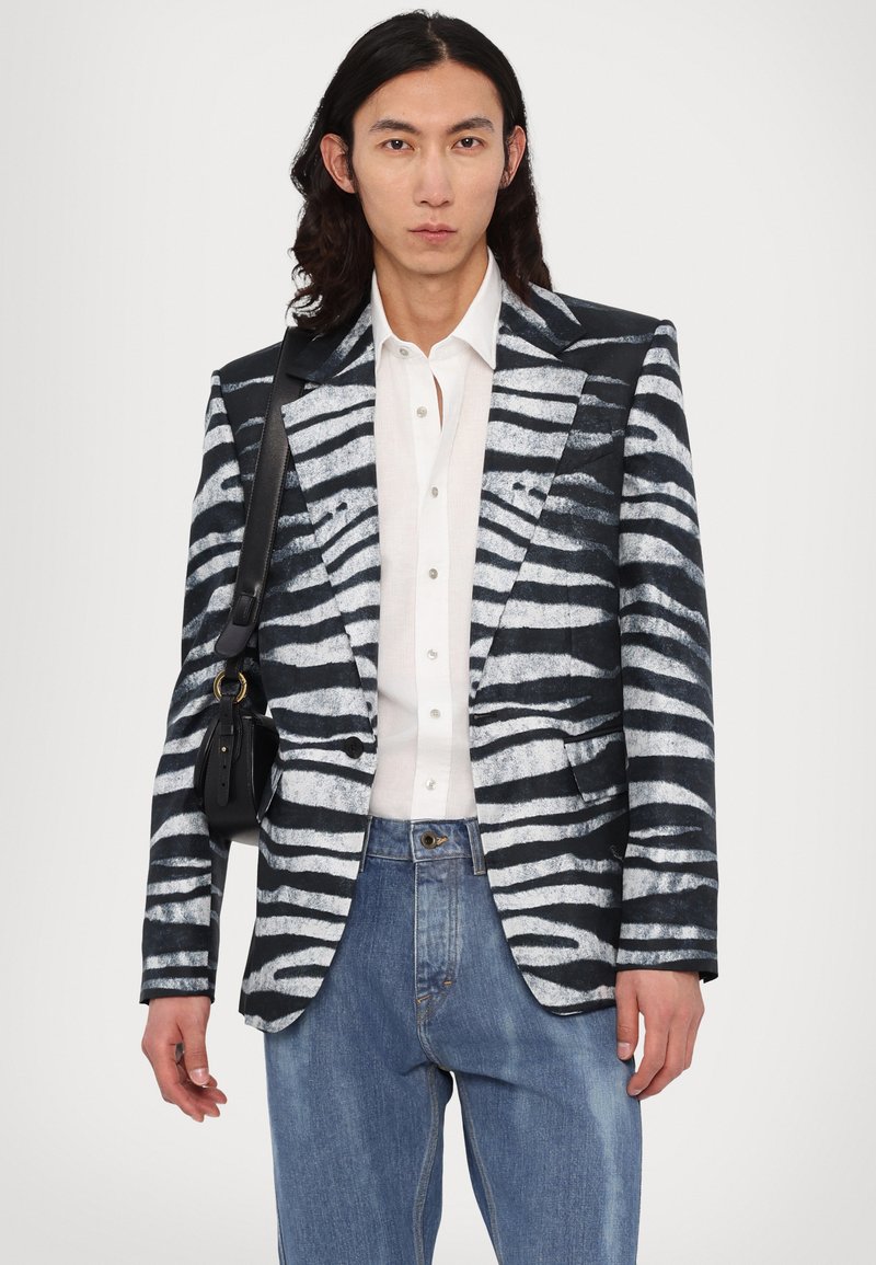 Sorte og hvide zebra-stribede blazer med en struktureret design, der har en spids krave og dobbelt knaplukning, parret med lyseblå denimbukser.