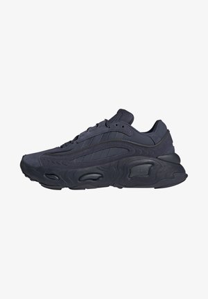 Baskets de sport noires avec semelle texturée, dessus en daim et tissu, et design à lacets, montrées de côté sur fond blanc.
