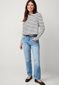 Gestreepte lange mouw top in zwart en wit, gecombineerd met lichtgekleurde rechte spijkerbroek. Zwarte platte schoenen maken de look compleet.