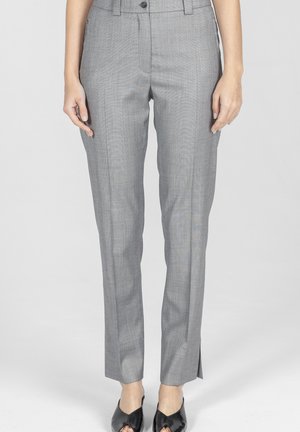 Kobieta nosząca dopasowane, jasnoszare spodnie z kantem z przodu i bocznymi rozcięciami, zestawione z czarnymi wsuwanymi butami z zaostrzonym noskiem.