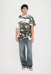 Camo-print oversized t-shirt in green, white, and brown; paired with light blue wide-leg jeans and black-and-white sneakers.