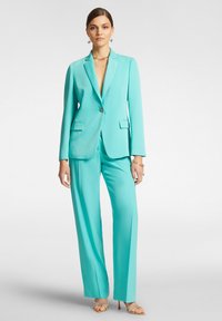 Blazer su misura turchese con bottone singolo, pantaloni a gamba larga coordinati, trama liscia e due tasche frontali, abbinati a tacchi a fascia.